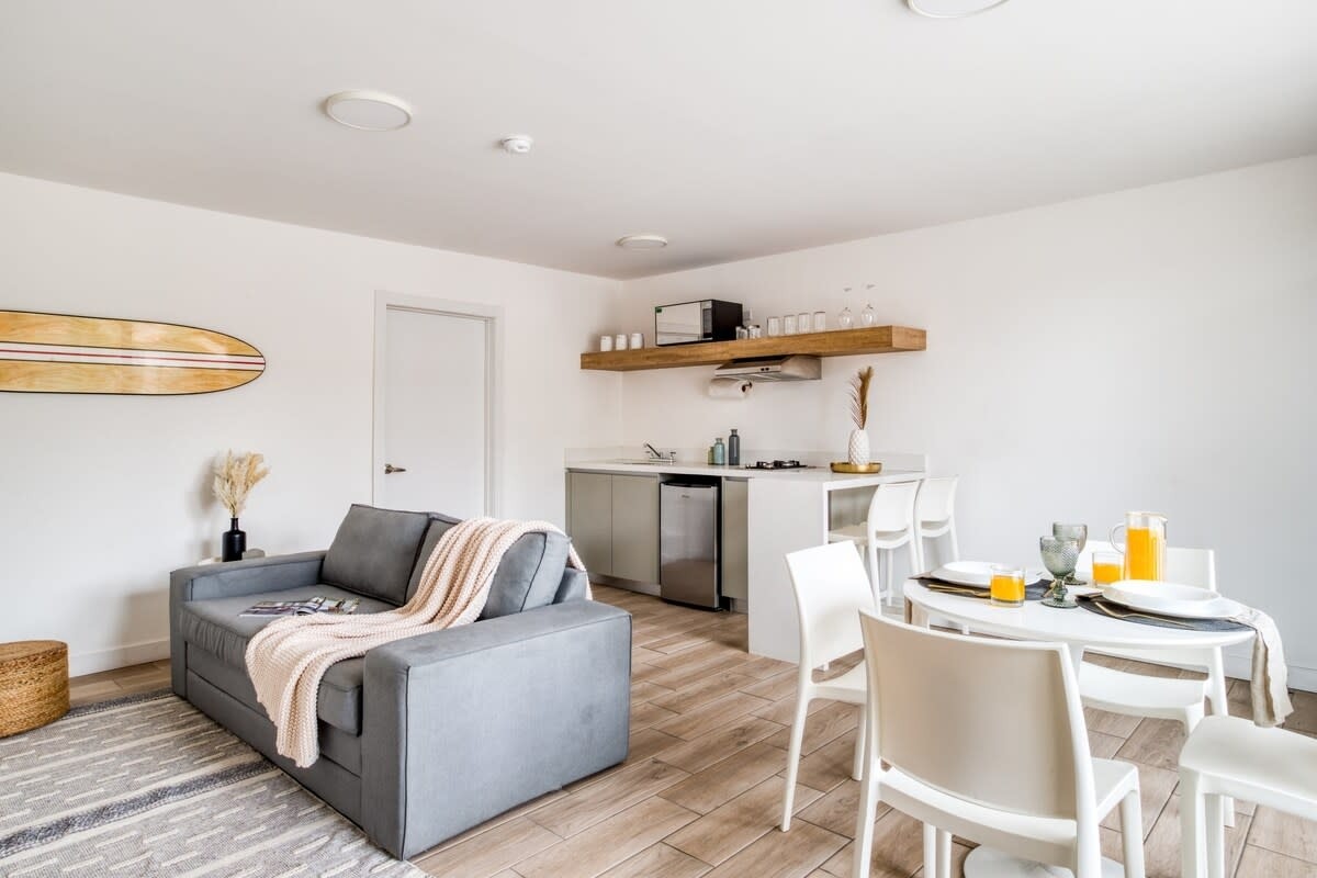 Bright coastal accommodation interior with a living area, dining table and kitchenette in Ensenada